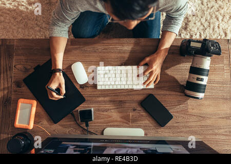 Vista superiore del fotografo editing di foto dopo un servizio fotografico con tavoletta grafica e penna stilo. Fotografo editing di foto sul computer desktop con una telecamera Foto Stock