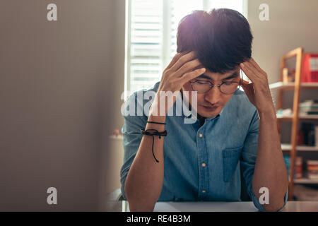 Uomo seduto alla sua scrivania cercando stressato e stanco. Uomo con testa in mani, cercando ha sottolineato a causa di un guasto. Foto Stock