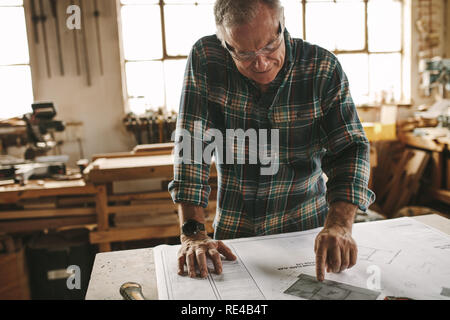 Carpentiere Senior studio del disegno prima di iniziare il suo lavoro in officina. Carpenter controllo disegno nel laboratorio di falegnameria. Foto Stock