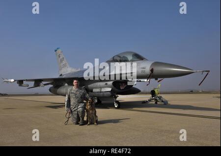 Il personale Sgt. Bryan Tarantella, 8 forze di sicurezza militari squadrone cane da lavoro gestore, si inginocchia davanti a un F-16 Fighting Falcon jet accanto a Stella, 8 Fs militari di cane da lavoro, sul flightline a Kunsan Air Base, Repubblica di Corea, nov. 11, 2016. La Tarantella è stato un gestore per undici anni e si appresta a passare alla Base Comune San Antonio- Lackland. Stella è giunta alla fine del suo servizio militare e andrà in pensione. Tarantella intende adottare Stella dopo il suo pensionamento. Foto Stock