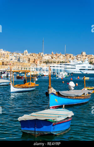 Tradizionali barche maltesi con superyacht in background con la Valletta visibile in background come visto da di Senglea, Malta Foto Stock