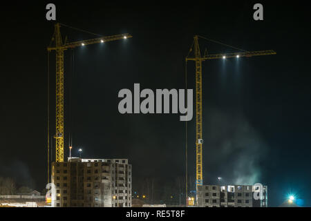 Gru a torre e incompiuta a più piani alto vicino a edifici in costruzione sito nella notte Foto Stock