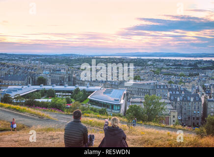 Una giovane donna è mostrando il suo amico maschio un bel tramonto sopra la città di Edimburgo dalla famosa Calton Hill. Foto Stock