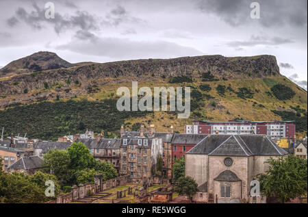 Un paesaggio urbano fotografia di Canongate Kirk, falesie e Arthur il mare nella città di Edimburgo in Scozia, Regno Unito su un nuvoloso giorno. Foto Stock