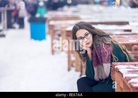 Ritratto di una donna bellissima con gli occhiali seduta a una coperta di neve la tabella in inverno Foto Stock