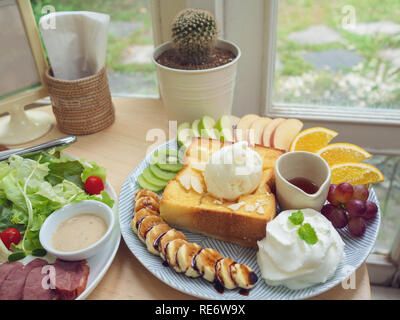 Il miele di appetitosi toast con gelato alla crema e frutta fresca servita con cotto Insalata di anatra sul tavolo di legno dalla finestra nel bellissimo cafe Foto Stock