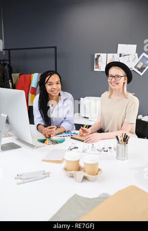 Ritratto di due sorridente designer di moda seduti a tavola disegno schizzi e lavorare con palette colorate in studio Foto Stock