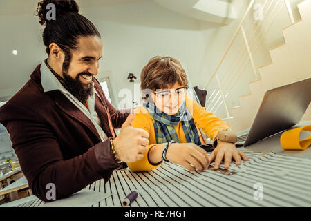 Padre barbuto sentirsi soddisfatto mentre suo figlio aiutandolo in atelier Foto Stock