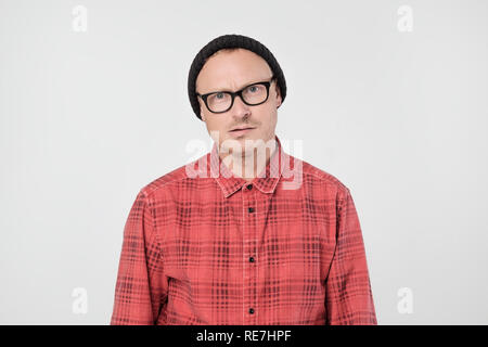 Giovane uomo europeo in maglietta rossa insoddisfatto acciglia e guarda sullenly. Foto Stock