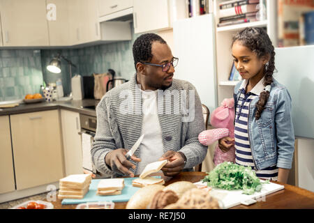 Poco carino figlia proveniente da cucina vedendo padre rendendo panini Foto Stock