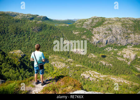 Escursionista in piedi sul Prekestolen e guardando sulla montagna accanto a Prekestolen in Norvegia Foto Stock