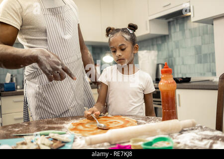 Padre indossando grembiuli a strisce ad insegnare la sua bambina rendendo la pizza Foto Stock