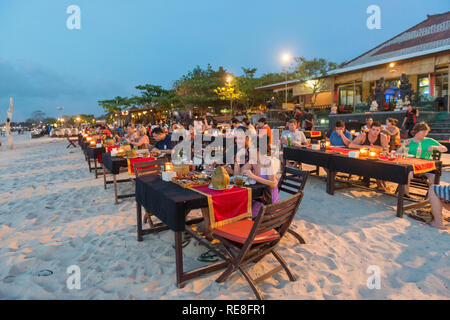 I turisti per gustare la cena sulla spiaggia di Jimbaran al crepuscolo. La spiaggia è famosa per i suoi ristoranti di pesce. Foto Stock