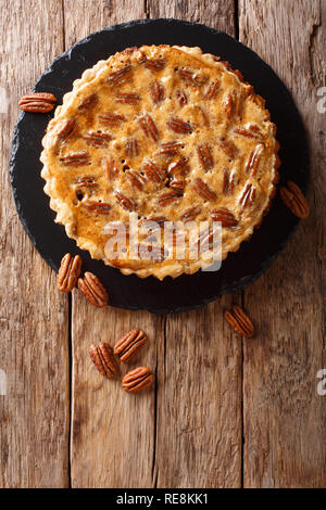 Gustosa torta alle noci pecan con cannella e caramello close-up su una scheda di ardesia sul tavolo. Verticale in alto vista da sopra Foto Stock