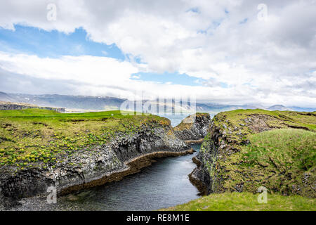 Vista del paesaggio di rocce di ponte nell'oceano sulla costa in Hellnar Parco Nazionale Penisola Snaefellsnes in Islanda con erba verde sul giorno di estate Foto Stock