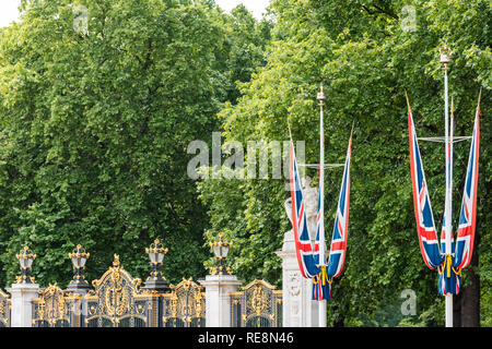London, Regno Unito - 21 Giugno 2018: Palazzo di Buckingham Gate recinzione architettura e bandiere durante la giornata estiva con verdi alberi in posizione di parcheggio Foto Stock