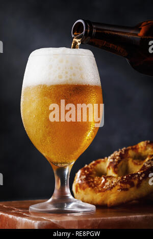 Bicchiere pieno di luce fresca birra con un pretzel su un piedistallo di pietra Foto Stock