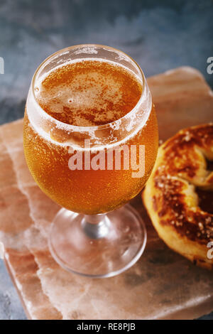 Bicchiere pieno di luce fresca birra con pretzel su un supporto pietra close-up Foto Stock