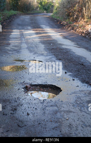 Buca nel paese strada nella campagna inglese. Strada asfaltata che necessitano di riparazione, la guida pericolosa superficie. Foto Stock