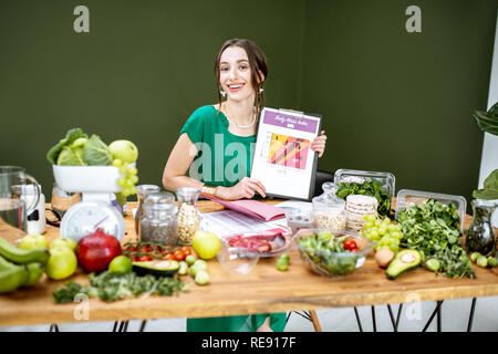 Ritratto di una donna bella come un dietista che mostra l'indice della massa del corpo schema seduta con vari cibi sani ingredienti nel verde office Foto Stock
