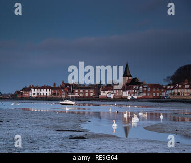 Bassa marea a Bosham quay con cigni bianchi che nuotano verso la telecamera, il campanile della chiesa che riflette in acqua calma Foto Stock