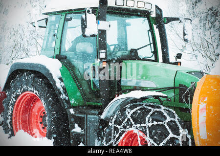 Pulizia del trattore di neve in campo. Vista ravvicinata di un trattore. Inverno Cleanining carrello nel villaggio. Verde con trattore rosso su strada Foto Stock