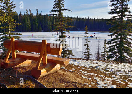 Un paesaggio invernale di un vuoto memorial panca su un belvedere che si affaccia sul Lago di Maxwell a Hinton Alberta in Canada con le persone che godono di un outdoor ska di ghiaccio Foto Stock