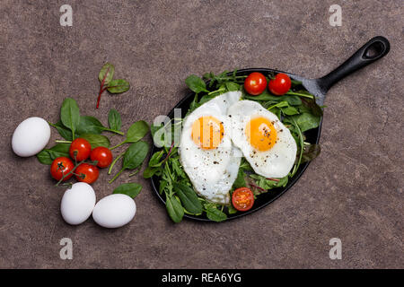 Concetto dello sfondo con uova fritte, pomodorini e fresco verde, rucola, spinaci con ingredienti a sfondo marrone. Concetto di lifesty sani Foto Stock