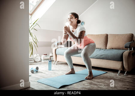 Sorridente curva lady facendo ampio squat durante il recupero in ordine Foto Stock