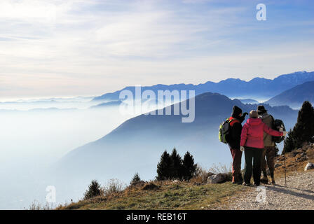 Altopiano di Asiago, Prealpi Venete, Italia. Tre gli escursionisti su un percorso. Sullo sfondo la Pianura Padana immersa nella smog. Foto Stock