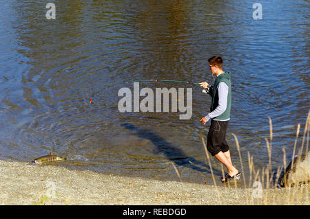 Ragazzo adolescente con canna da pesca e un pesce sulla banca del fiume di Alouette in Maple Ridge, British Columbia, Canada Foto Stock