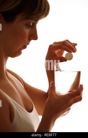 Giovane donna sciogliendo una compressa in un bicchiere di acqua Foto Stock