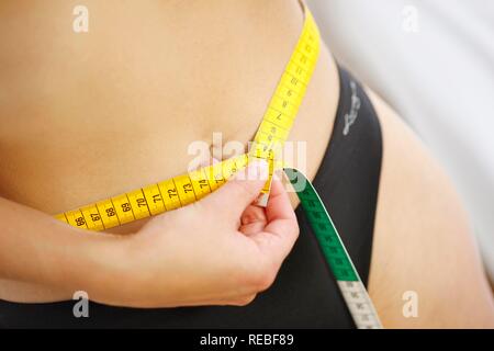 Giovane donna misurando la sua circonferenza addominale, alla cintura, con un nastro di misurazione Foto Stock