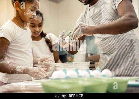 Funny ragazze con facce in farina guardare il loro padre Battere le uova Foto Stock