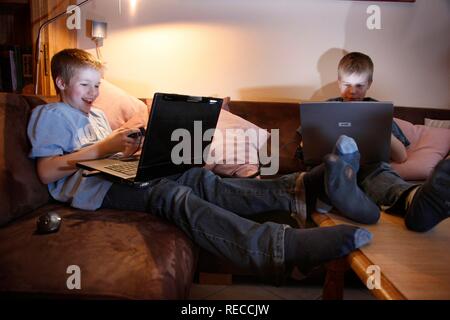 Fratelli, 11 e 13 anni, con computer portatile nel soggiorno, la riproduzione di un auto da corsa gioco per computer su due computer Foto Stock