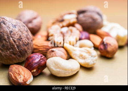 Mandorle, Nocciole, Noci di acagiù e noci intere su sfondo dorato. Sani Snack organico, colazione, ingredienti alimentari Foto Stock