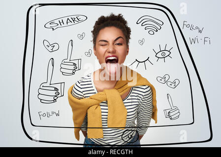 Giovane donna studio isolato permanente nel muro bianco inclinato in avanti con una strizzatina d'occhio che mostra la linguetta giocoso close-up Foto Stock