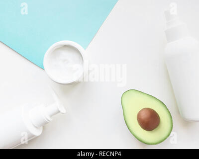 Diversi prodotti cosmetici in bianco bottiglie, vasetti e una metà di avocado sono giacenti su due toni del modello dello sfondo per poster e insegne Foto Stock