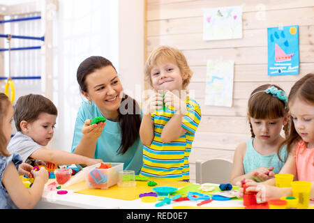 I bambini giocano di pasta in asilo nido. I bambini con insegnante lo stampo da plastilina in asilo nido. Poco gli studenti impastare la creta per modellare con le mani in età prescolare. Foto Stock