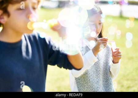 Poco ragazza asiatica e caucasico ragazzo giocando insieme soffiando bolle di sapone all'aperto in un parco. Foto Stock