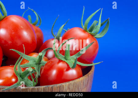 Rossi freschi maturi pomodori ciliegia in piccola ciotola di legno su sfondo blu Foto Stock