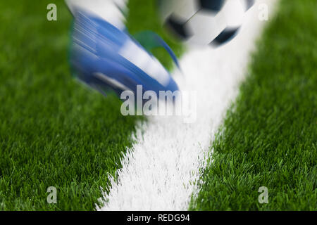 Giocatore di calcio di sparare un pallone da calcio con i suoi piedi sul campo di calcio. Piedi e palla in movimento. Calcio sfondo dettaglio Foto Stock