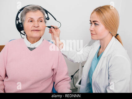 Senior paziente che indossa le cuffie, seduta vicino audiologist durante l orecchio esame presso una clinica di audizione Foto Stock