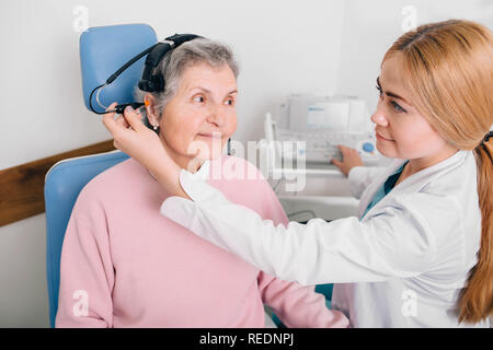 Senior paziente che indossa le cuffie, seduta vicino audiologist durante l orecchio esame presso una clinica di audizione Foto Stock