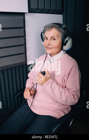 Senior paziente che indossa le cuffie, seduto in cabina insonorizzata, durante l'esame dell'orecchio a audiologi office Foto Stock