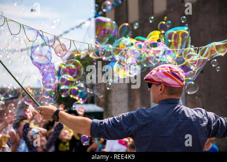 Un clown freelance soffiando centinaia di minuscoli, piccole e grandi bolle a festival all'aperto nel centro citta'. Concetto di intrattenimento, compleanni. I bambini aventi Foto Stock