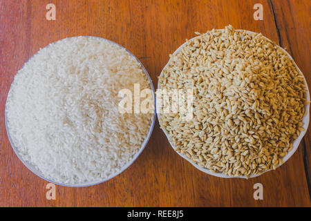 Lucidato e paddy o unhusked riso in due piastre vicino sul tavolo di legno sfondo Foto Stock