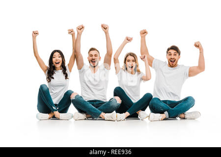 Entusiasti giovani amici in bianco t-shirts seduto e alzando le mani isolato su bianco Foto Stock