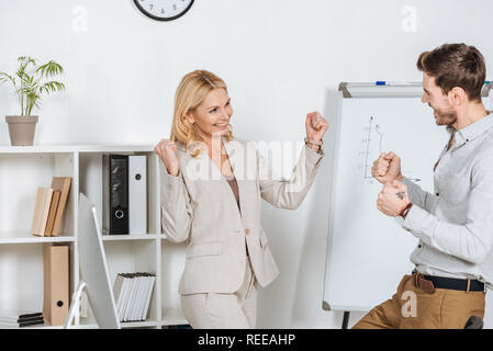 Eccitato giovane imprenditore e imprenditrice matura in trionfo e scuotendo i pugni in office Foto Stock