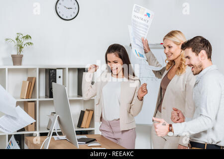 Imprenditori eccitati agitando i pugni e guardando il desktop computer in ufficio Foto Stock